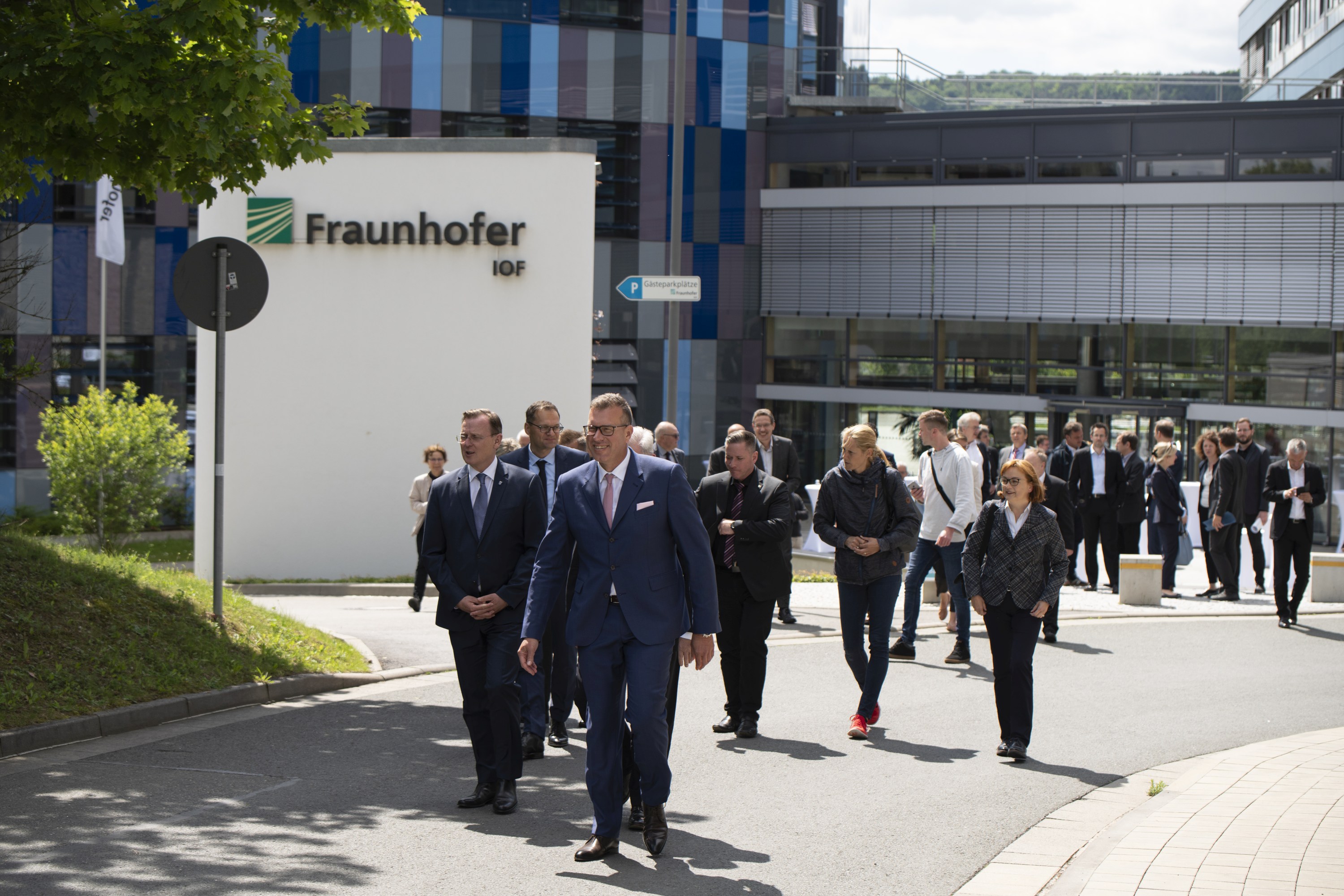 Gruppe von Männern und Frauen in formeller Kleidung gehen eine Straße entlang, im Hintergrund das Fraunhofer-Institut für Angewandte Optik und Feinmechanik